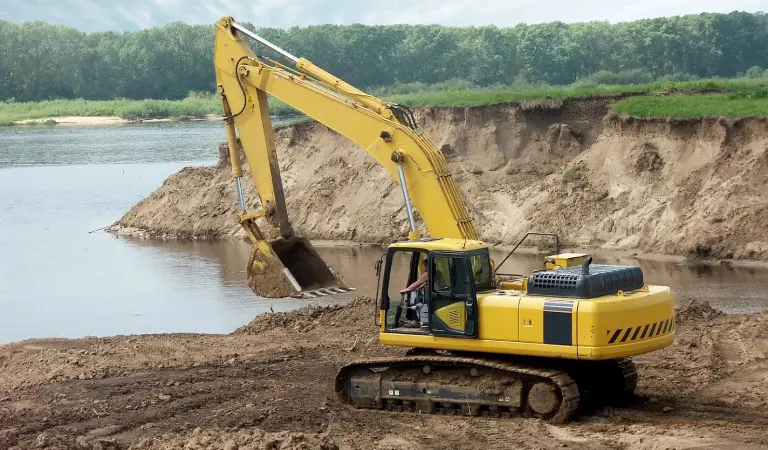 A yellow and black excavator on dirt field near water.