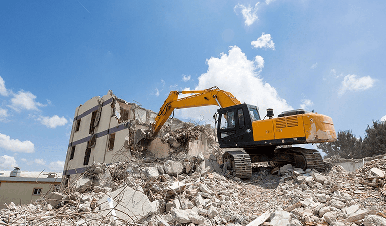 A yellow and black excavator is on the rubble