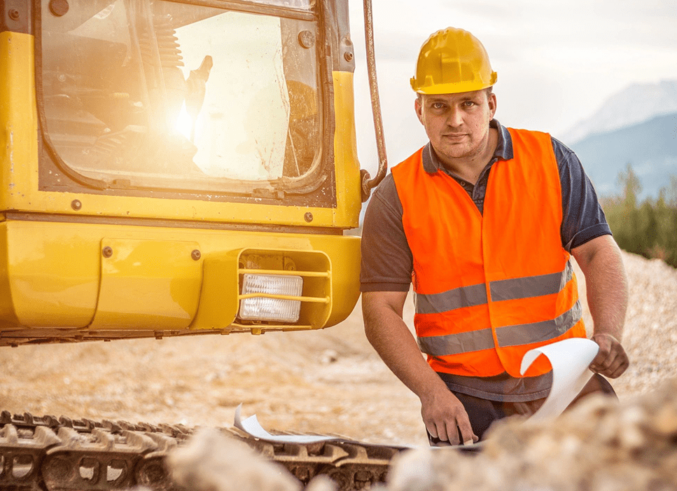 A man in an orange vest and hard hat standing next to a yellow construction vehicle.