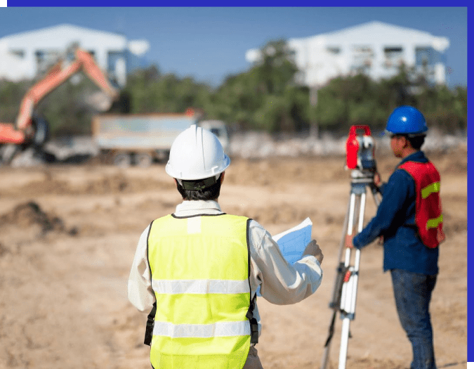 Two men in hard hats and safety vests are standing on a construction site.